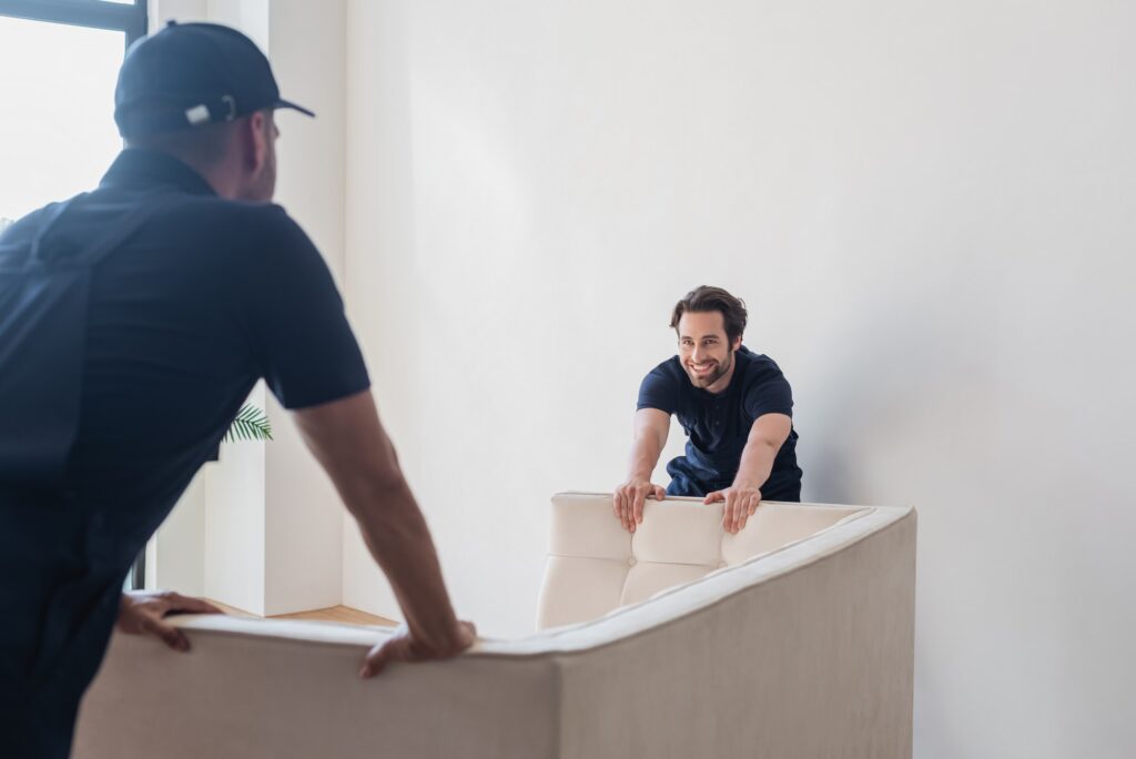 smiling worker moving white sofa with blurred colleague